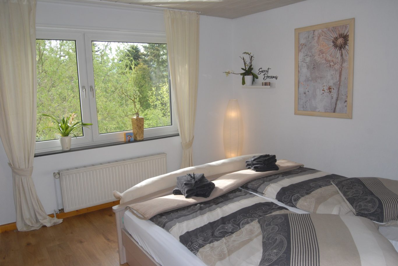 Helles Schlafzimmer mit zwei Betten, Pflanzen am Fenster und einem dekorativen Bild an der Wand.