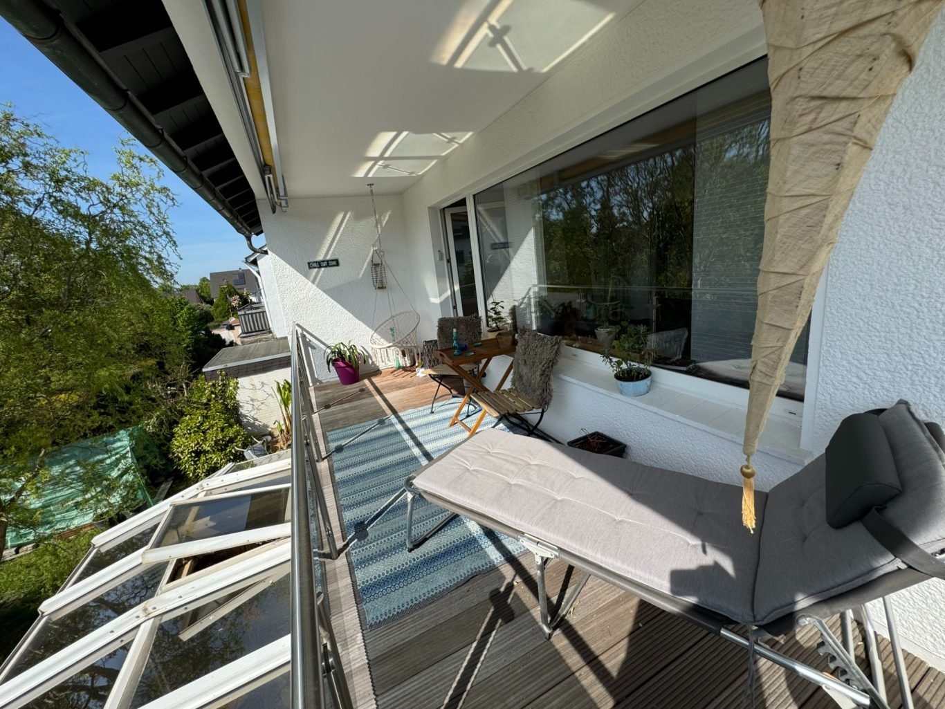Balkon mit Tisch und Stühlen, umgeben von Bäumen und Sonnenschein.