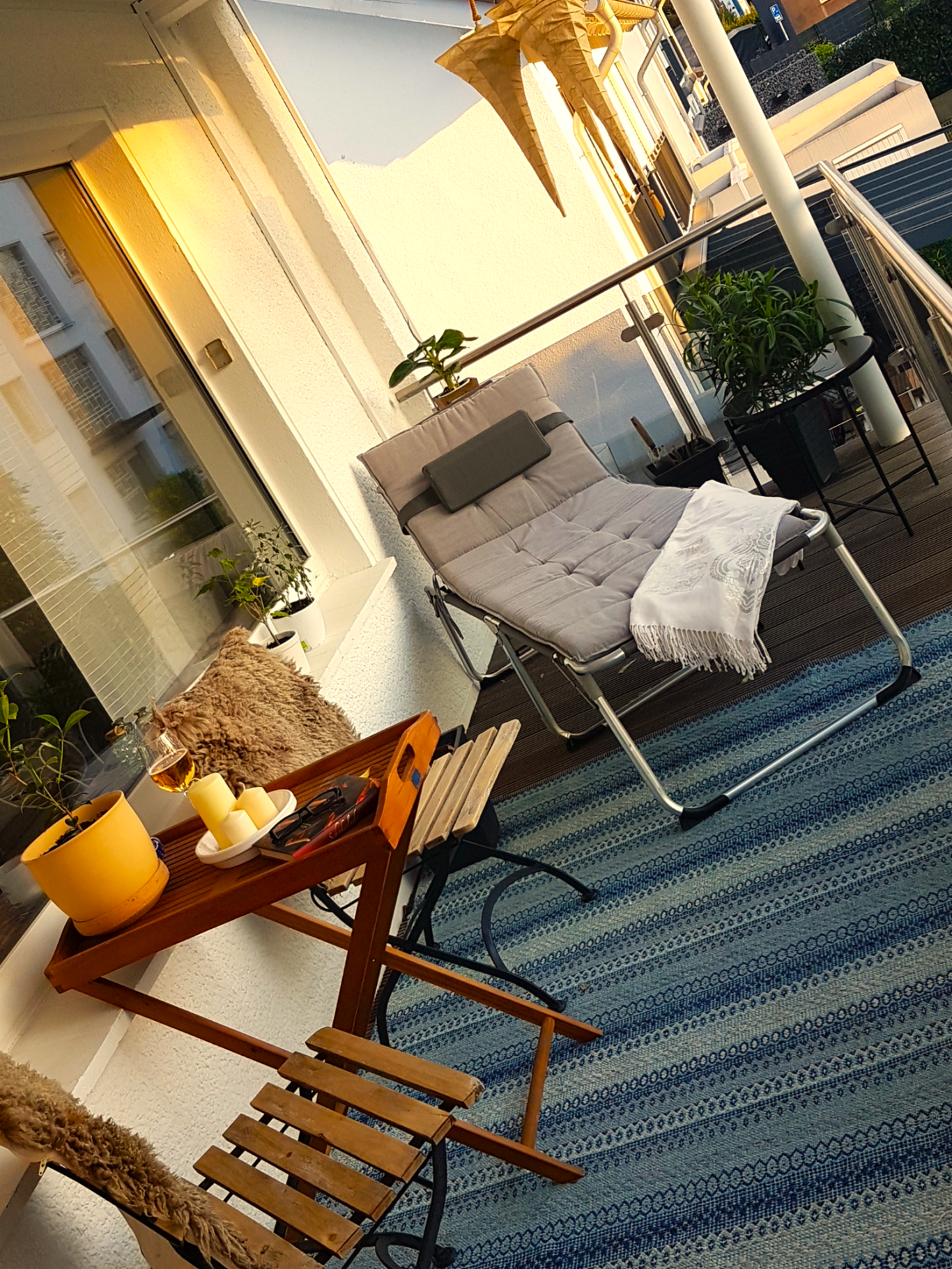 Gemütlicher Balkon mit Liegestuhl, Tisch, Pflanzen und warmem Licht.