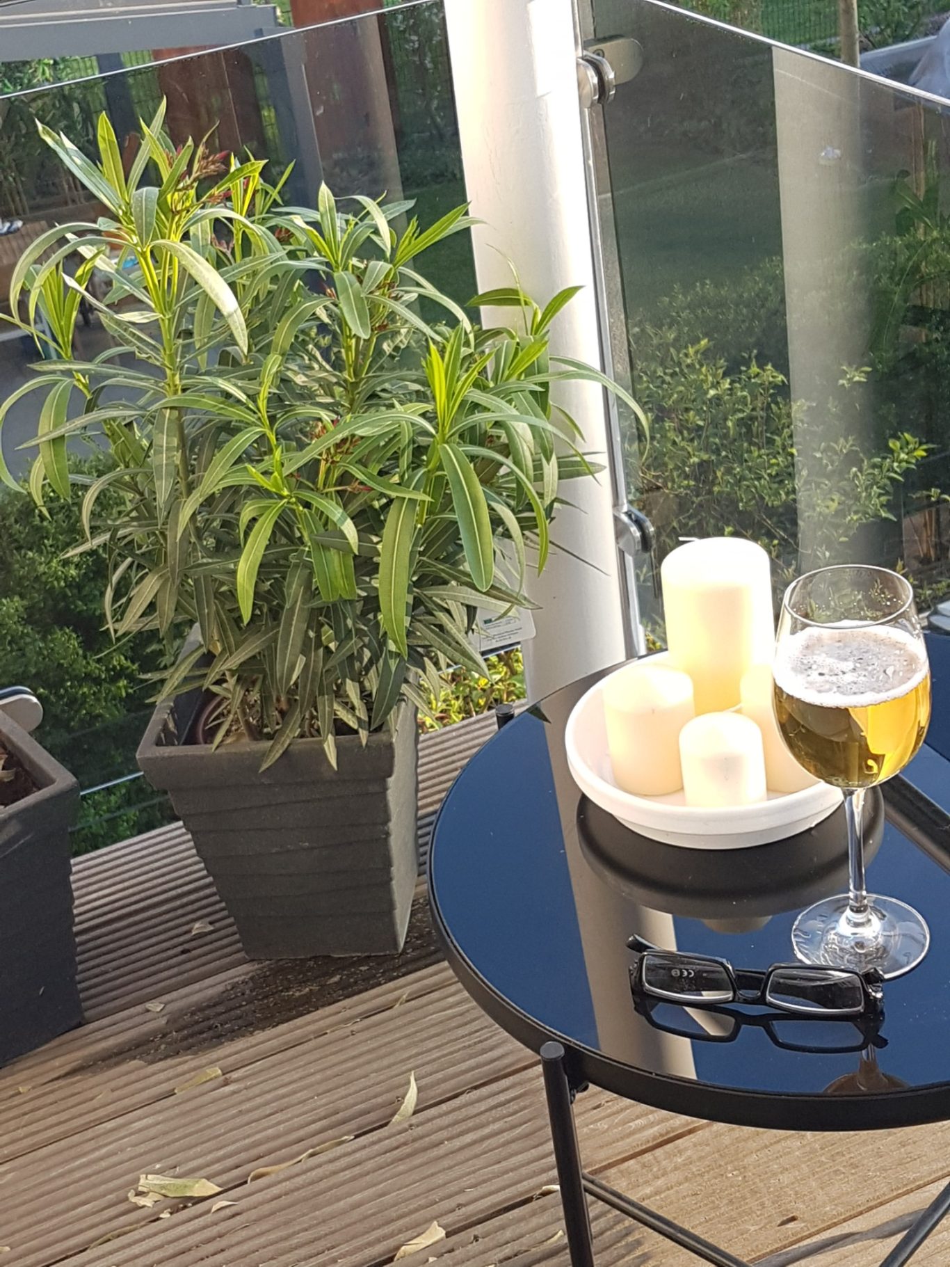 Ein Tisch mit einer Pflanze, Kerzen und einem Glas Bier auf einem Balkon.