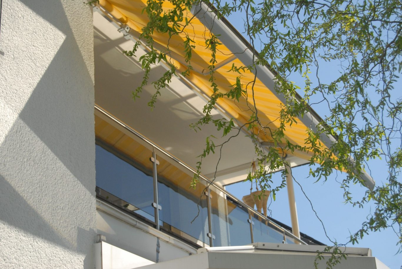 Moderne Architektur mit gelbem Sonnenschutz und grünen Pflanzen im Vordergrund.