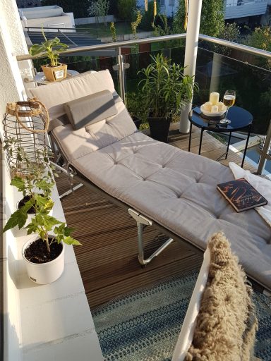 Bequeme Liege auf einem Balkon, umgeben von Pflanzen und einem kleinen Tisch mit Getränken.