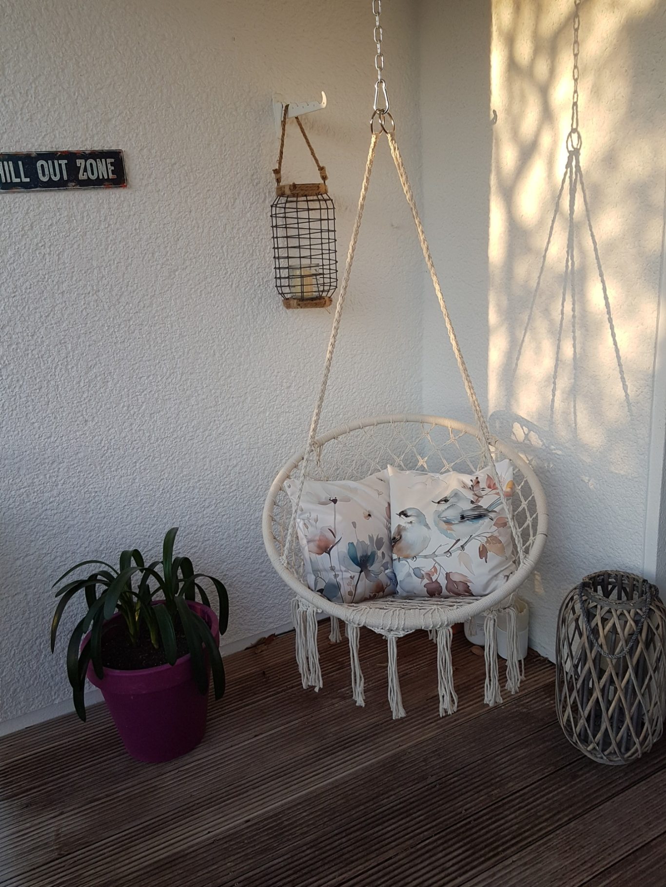 Chill Out Zone Hängesessel mit Kissen in einer Ecke mit Pflanzen und dekorativen Elementen.