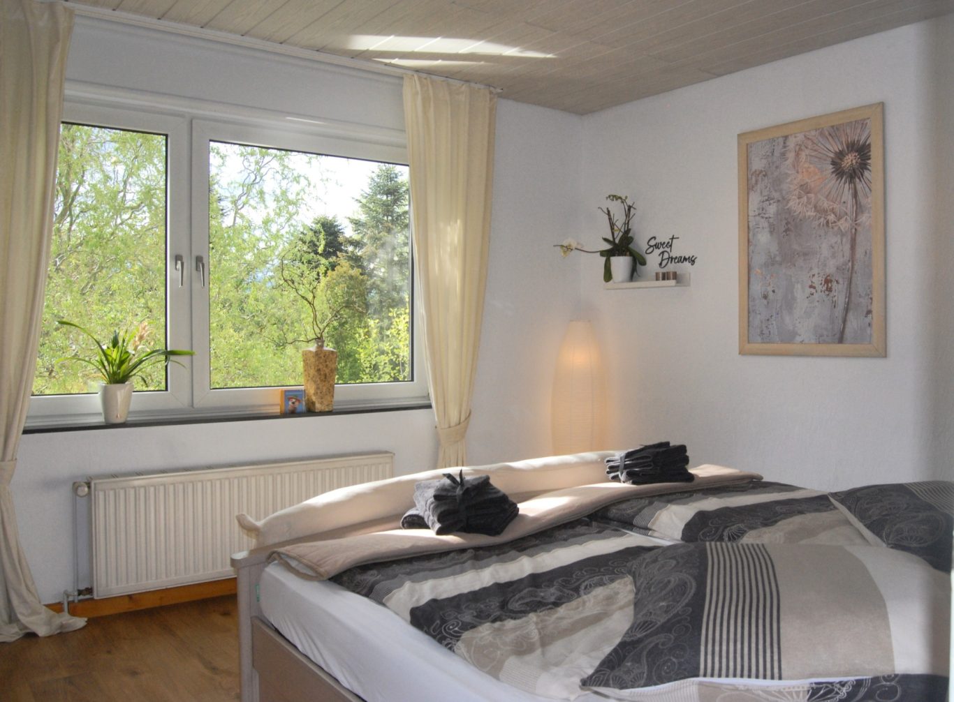 Naturnah Helles Schlafzimmer mit Bett, Pflanzen und großer Fensterfront zur Natur.